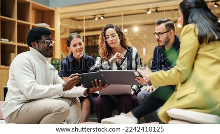 Group of People from Multiple Ethnicities Working on Problem Solving Using Notes, Laptop and Tablet in a Meeting Room at the Office. Teammates Giving Constructive Feedback on Eachother's Projects Royalty-Free Stock Photo #2242410125
