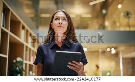 Close Up of a Content Female CEO Making Notes on her Tablet. Portrait of a Caucasian Woman Crossing a Corporate Office Hall, Smiling and Looking Confident. Low Angle Royalty-Free Stock Photo #2242410177