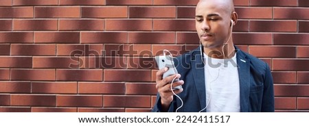 Music lover. Young guy wearing earphones standing on wall listening to music on smartphone serious