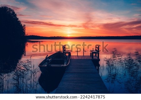 Sunset on a lake. Wooden pier with fishing boat at sunset in Finland. Beautiful summer landscape.