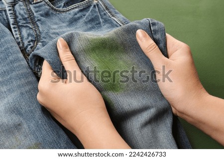 Woman holding jeans with stain on green background, closeup Royalty-Free Stock Photo #2242426733