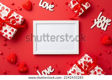 Valentine's Day concept. Top view photo of white photo frame gift boxes heart shaped candles inscriptions love and sprinkles on isolated red background with blank space