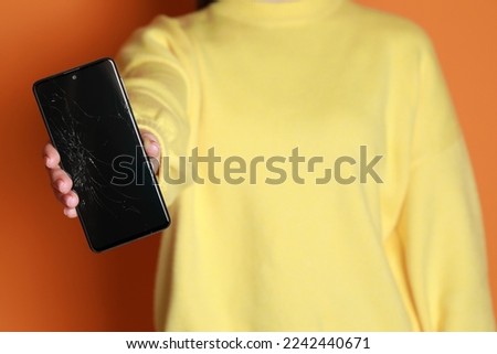 Woman showing damaged smartphone on orange background, closeup. Device repairing