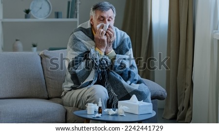 Sick elderly man covered with warm blanket suffer from runny nose sneezes in napkin unwell old grandpa feeling bad fever virus illness symptoms senior male have health problem covid19 epidemic concept Royalty-Free Stock Photo #2242441729