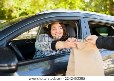 Cheerful obese woman smiling while buying fast food at a drive thru while driving her car  Royalty-Free Stock Photo #2242453385