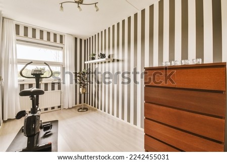 a living room with black and white striped wallpapers on the walls, an exercise bike in the corner Royalty-Free Stock Photo #2242455031