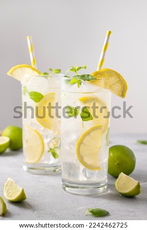 Mojito drink with fresh lemons. Refreshing cocktail with lime, lemon, mint and ice in a tall glass on gray background. Summer cold drinks concept. Front view.