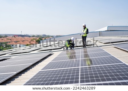 Engineer on rooftop kneeling next to solar panels photo voltaic with tool in hand for installation Royalty-Free Stock Photo #2242463289