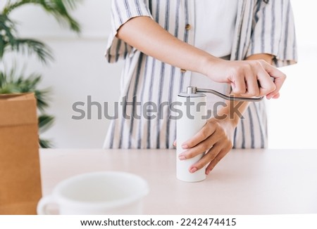 Crop video of a woman using white color hand coffee grinders on the table before making pour-over on ground coffee over the paper filter on a glass dripper. An alternative method is called Dripping.