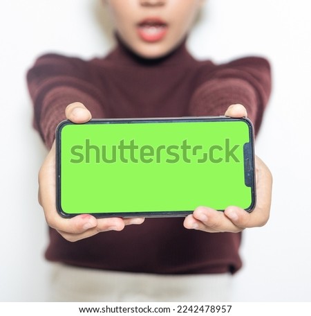 A woman holding a smartphone with green colored screen while surprised on the white background