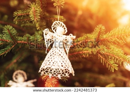 Knitted toy angel on a fir tree in sunlight. Christmas concept. Closeup.