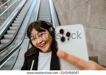Young asian woman taking selfie photo on cellphone and holding coffee while riding escalator