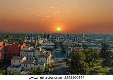 aerial shot along Raymond Ave with lush green trees, grass and plants and red brick buildings with cars driving on the street with powerful clouds at sunset in Pasadena California USA Royalty-Free Stock Photo #2242500649