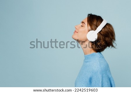 Young happy fun caucasian woman wear knitted sweater headphones listen to music with closed eyes have fun isolated on plain pastel light blue cyan background studio portrait. People lifestyle concept Royalty-Free Stock Photo #2242519603