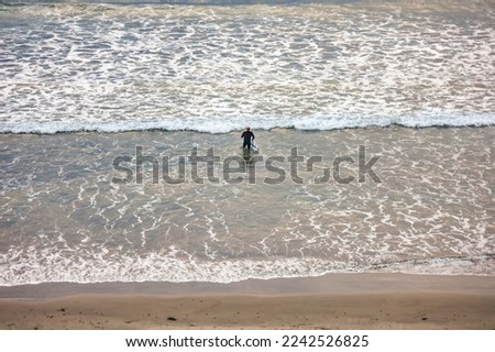 View of an adult male surfer holding his surfboard walking into the ocean water. 