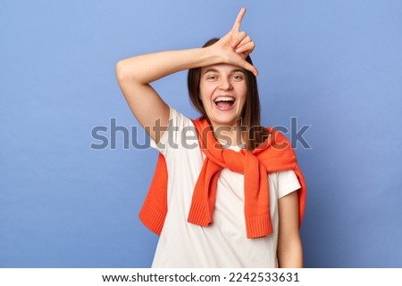 Image of happy positive excited Caucasian woman wearing casual style clothing standing isolated over blue background, showing shaka gesture in front her forehead.