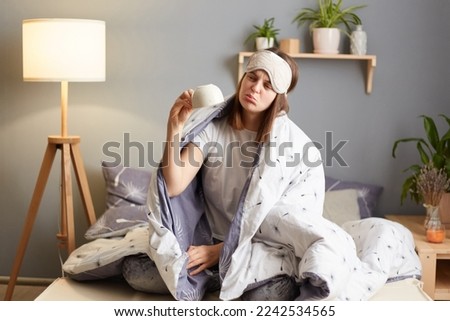 Early morning wake up. Portrait of woman in pajamas on bed, wrapped in warmth cozy blanket, raise hand with upside empty coffee cup, needs energy, being sad and upset.