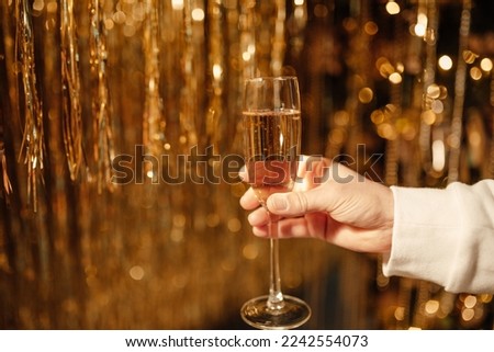 Male hand holds flute glass with bubbly wine at sparkling bokeh yellowish golden sequin garlands blaze. Bright falling gold glitter ribbons glittering twinkle decoration for celebrating luxury party
