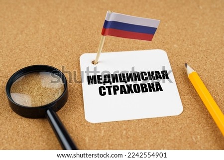 On the table is the flag of Russia, a pencil, a magnifying glass and a sheet of paper with an inscription in Russian, which translates into English as - Health insurance