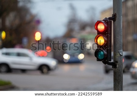 blurred city traffic with traffic lights, in the foreground a semaphore with a red and orange light
