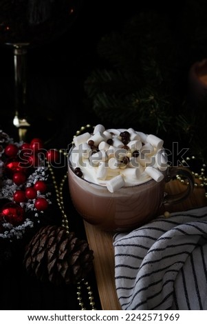 Big mug of hot chocolate wit marshmallows on wooden desk. Black back ground. pine cone and golden beads for decoration. Dark and moody stock food photography.