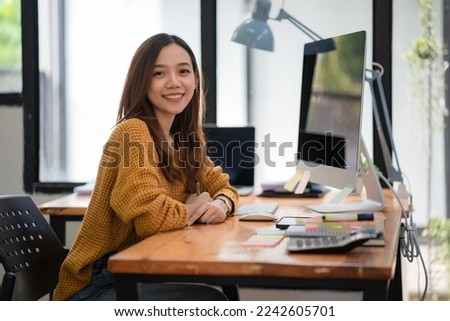 Portrait of a Beautiful Asian freelancer Using Desktop Computer at the home office. Smiling and looking at the camera.
