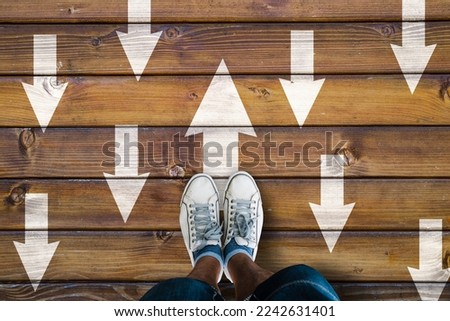 man sneakers and opposing direction arrows on wooden floor, personal perspective footsie concept for finding your own way