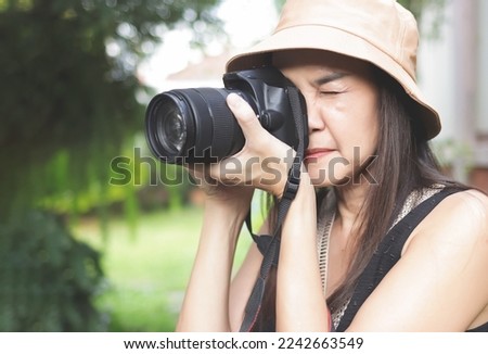 Close up image of Asian woman wearing hat and sleeveless top  taking photos in the park with dslr camera.  