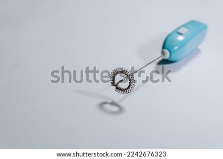 Blue handheld milk frother made of plastic. Portable mini foam maker for a latte, cappuccino, or hot chocolate on isolated white and blurred background.