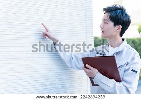 Japanese man examining the wall of the house Royalty-Free Stock Photo #2242694239