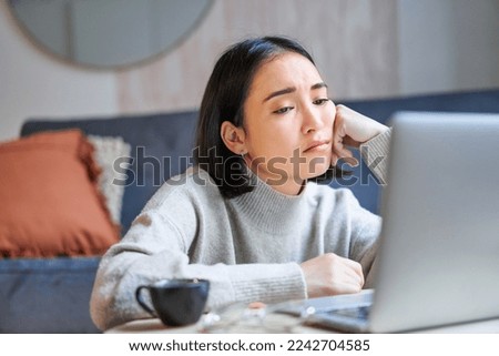 Portrait of korean girl sits bored, student looks gloomy at laptop, sitting at home and expressing boredom.