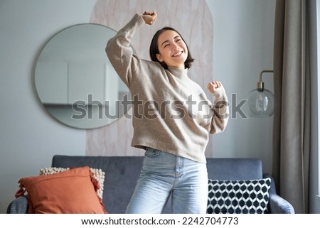 Portrait of happy asian woman dancing, rejoicing and triumphing, feeling upbeat at home. Copy space Royalty-Free Stock Photo #2242704773