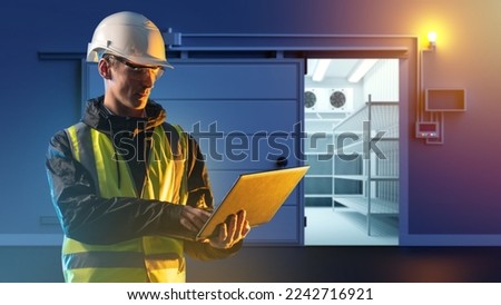 Industrial warehouse worker. Man with laptop near large refrigerator. Industrial refrigerator behind guy. Worker in reflective vest and protective helmet. Man operates refrigerator through laptop Royalty-Free Stock Photo #2242716921