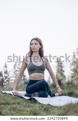 Flexible girl doing yoga in mountains among the fir trees on sunny day