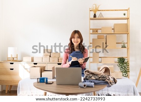 Woman runs an e-commerce business is writing a list of customers on paper before shipping to them, Business woman runs an e-commerce business on websites and social media. Selling products online. Royalty-Free Stock Photo #2242733993