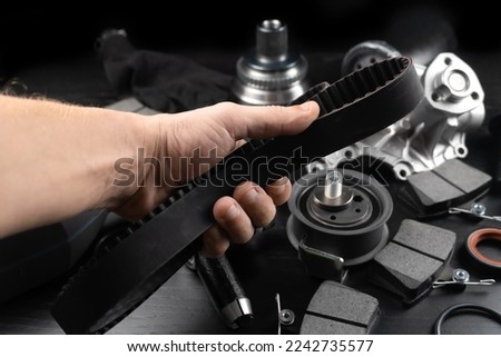Timing belt and tension rollers of gas distribution system of car engine, concept of car maintenance. Master's hand holds timing belt against background of spare parts. Royalty-Free Stock Photo #2242735577