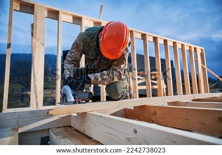 Carpenter using circular saw for cutting wooden plank. Man worker building wooden frame house. Carpentry concept. Royalty-Free Stock Photo #2242738023