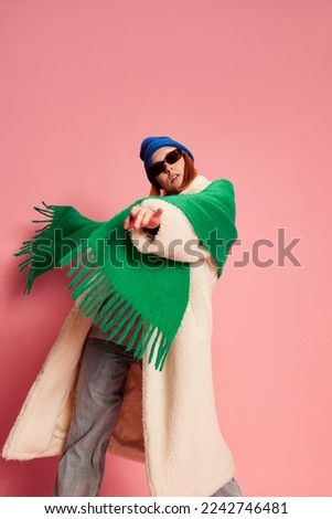 Emotie, stylish young girl in sunglasses, blue hat, green scarf and fur coat posing over pink background. Concept of youth, beauty, winter fashion, lifestyle, emotions, facial expression. Ad