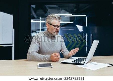 Senior gray haired businessman in office frustrated and sad trying to make bank transaction and purchase in online internet store, man holding bank credit card and using laptop. Royalty-Free Stock Photo #2242752831