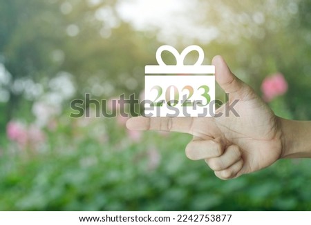 Gift box happy new year 2023 flat icon on finger over blur pink flower and tree in park, Business shopping online concept