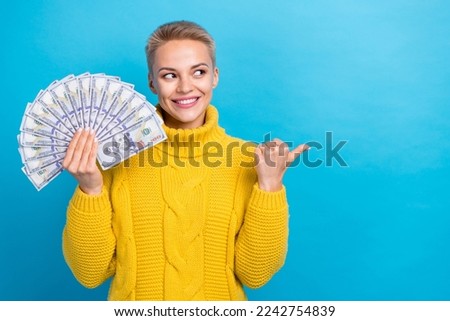 Photo of rich businesswoman wear yellow sweater hold usd look finger indicate empty space new gambling lottery isolated on blue color background