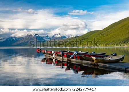 Motorboats lined up on a dock reflected in a beautiful lake with snow-capped mountains in the background at Lake McDonald in Glacier National Park Royalty-Free Stock Photo #2242779417