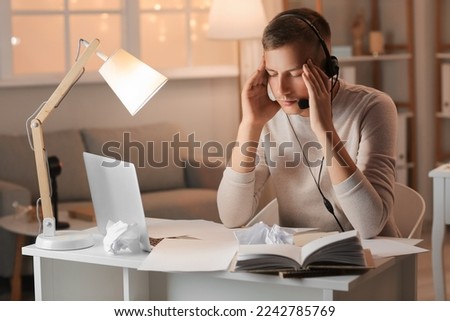 Tired young man with headset studying online at home late in evening