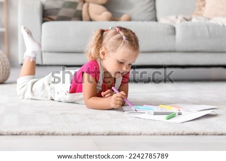 Cute little girl drawing with felt-tip pen on floor at home