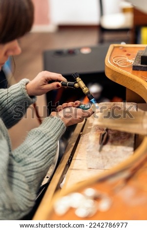 Stock photo of concentrated woman using blowtorch in jewelry workshop.