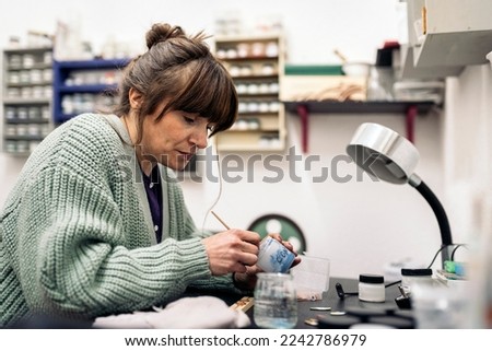 Stock photo of adult woman using paint in jewelry workshop.