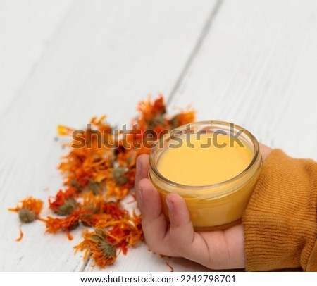 Boy´s hand holdind calendula ointment, copy space. Medicinal cream from dried marigold flowers good for skin. White wooden table. 