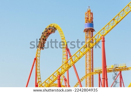 Roller coaster up down turn and a passing loop feint, spiral train of trolleys tends to go down, tower with free fall chairs nearby Royalty-Free Stock Photo #2242804935