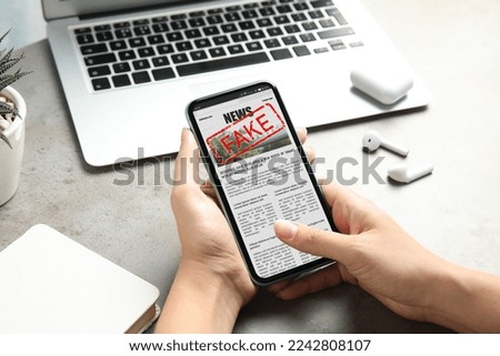 Fake information. Woman using mobile phone to read news at table, closeup Royalty-Free Stock Photo #2242808107