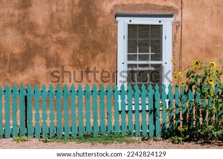Sunflowers and turquoise color wood fence set in front of a window and old adobe wall along Canyon Road in Santa Fe, New Mexico
